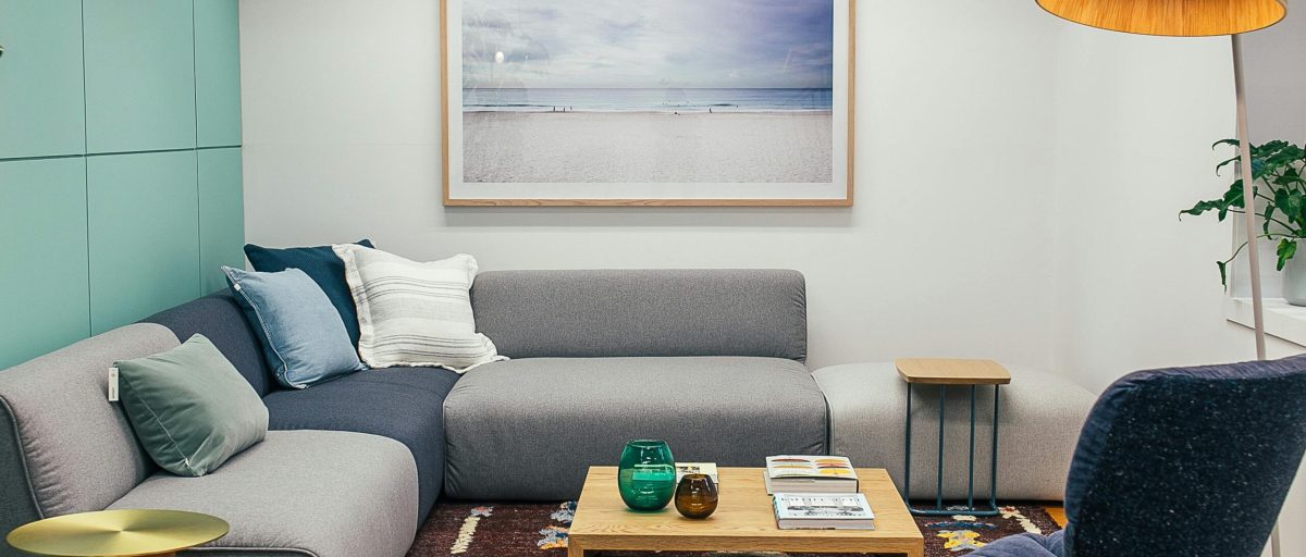 Soft gray sofa with cushions and wooden coffee table placed near armchair in living room with floor lamp and painting on wall