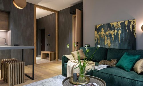 Stylish living room featuring a green velvet sofa, abstract art, and a cat lounging comfortably.